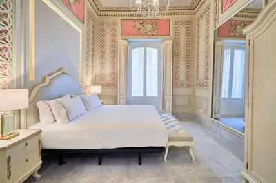a bedroom with a large bed and a chandelier at Tandem Palacio Veedor de Galeras Suites in Cádiz