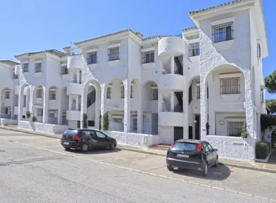 two cars parked in front of a large white building at Apartamento la Barrosa ,Urb los Veleros in Chiclana de la Frontera