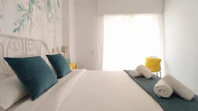 a bedroom with a white bed with blue pillows and a window at AZAHAR-Playa Home by Cadiz4Rentals in Cádiz