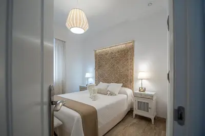 a white bedroom with a bed and a lamp at Apartamento Garum in Cádiz