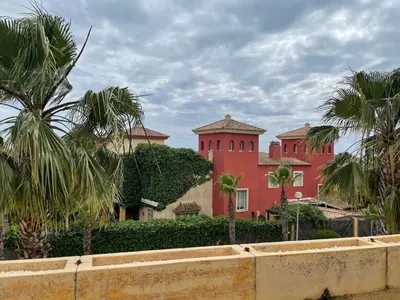 a red building with palm trees in front of it at Playa las Redes in El Puerto de Santa María