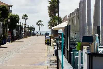 a street with tables and chairs and palm trees at R&B Puerto Sherry Beach in El Puerto de Santa María