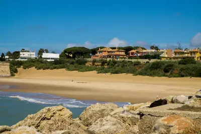 a sandy beach with houses in the background at R&B Puerto Sherry Beach in El Puerto de Santa María