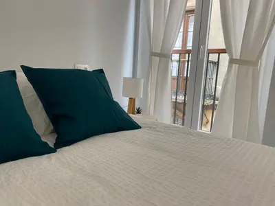 a white bed with green pillows and a window at Cartujano City Center Apartment in Jerez de la Frontera