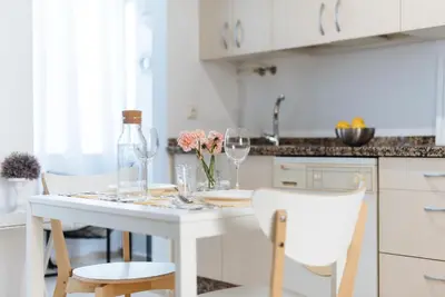 a white kitchen with a table with wine glasses and flowers at LyriosHomes Chipiona Beach in Chipiona