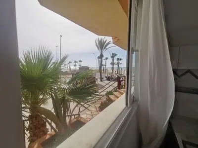 a window with a view of the beach and palm trees at Apartamentos Sanlúcar Beach 2 y 3 in Sanlúcar de Barrameda