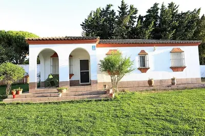 a small white house with a grass yard at Chalet con piscina, amplio jardin y aire acondicionado in Chiclana de la Frontera