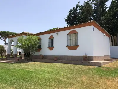 a white house with windows and a yard at Chalet con piscina, amplio jardin y aire acondicionado in Chiclana de la Frontera