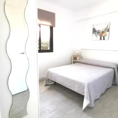 a white bedroom with a bed and a window at Brisa marina novo sancti petri in Chiclana de la Frontera
