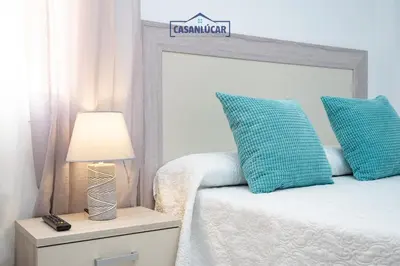 a bed with blue pillows and a lamp on a night stand at Piso Nao Victoria in Sanlúcar de Barrameda