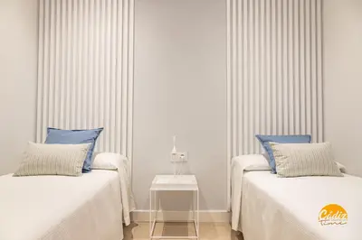 two beds in a white room with blue pillows at Villalobos by Cadiz Time in Cádiz