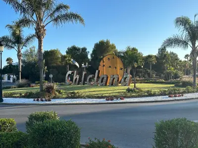 a sign for a church in a park with palm trees at En la zona más tranquila del Novo Sancti Petri in Chiclana de la Frontera