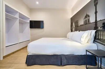 a bedroom with a large white bed and a television at Tandem Pópulo in Cádiz