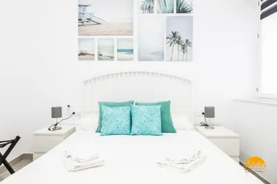 a white bedroom with a white bed with blue pillows at El Arco del Fotografo by Cadiz Time in Cádiz