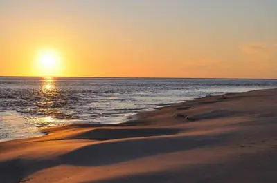 a beach with the sun setting over the ocean at Cañailla in San Fernando