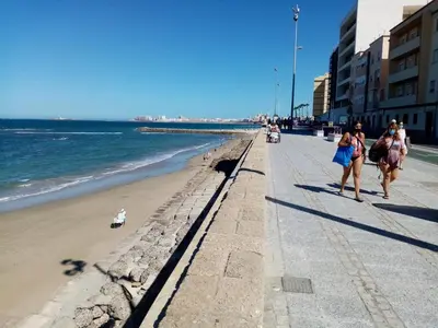 two women walking on the beach near the ocean at Paseo marítimo de Cádiz in Cádiz