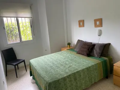 a bedroom with a bed and a chair and a window at Apartamento jardin Sanlucar in Sanlúcar de Barrameda