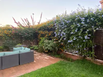 a garden with a hedge with purple flowers and a couch at Apartamento jardin Sanlucar in Sanlúcar de Barrameda
