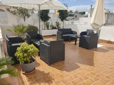 a patio with chairs and tables and an umbrella at Apartamento la Capillita in Sanlúcar de Barrameda
