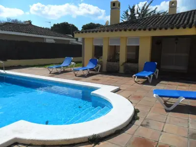 a swimming pool with blue chairs next to a house at Villas Aloha Valdelagrana in El Puerto de Santa María