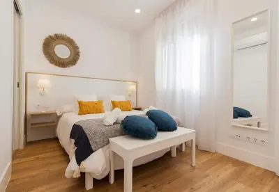 a white bedroom with a large bed with blue pillows at Apartamento Barrocal in Cádiz