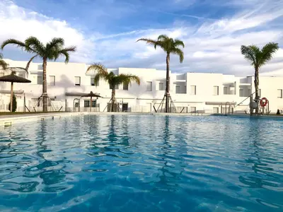 a swimming pool in front of a white building with palm trees at GATU PREMIUM Conil Sunset house con piscina, 3 dormit, 3 baños, jardín privado , wifi y parking, preferente mayores de 21 años y familias in Conil de la Frontera