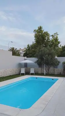 a blue swimming pool with two chairs and an umbrella at Casa grande con piscina in Rota
