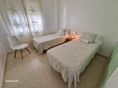 a small bedroom with two beds and a chair at Guadalquivir amplio y céntrico in Sanlúcar de Barrameda