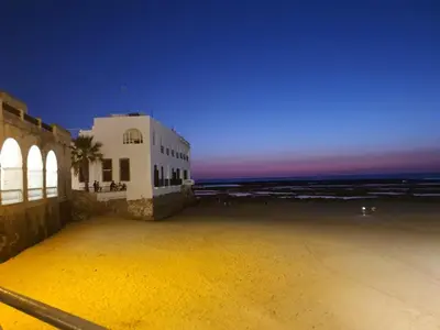 a building on a beach with the ocean at night at Apartamento en la playa cruz del mar chipiona in Chipiona