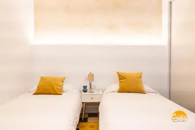 two beds in a room with white walls and yellow pillows at La Casa del Alfarero by Cadiz Time in Cádiz