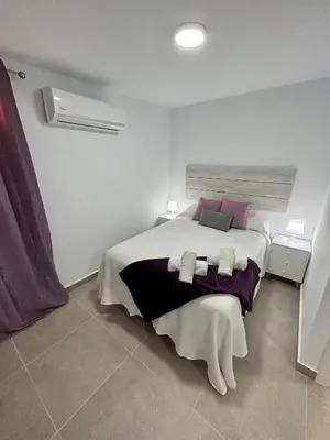 a white bedroom with a large bed with purple pillows at Apartamentos Los Cabezuelos, Dream Views in Arcos de la Frontera