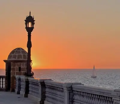 a street light next to the ocean with a sailboat at El rincón de la Caleta in Cádiz