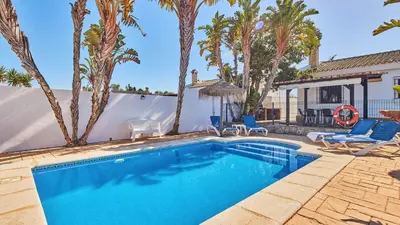 a swimming pool with chairs and a house with palm trees at Chalet La Raya Conil de la Frontera by Ruralidays in Conil de la Frontera