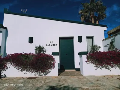 a white building with a green door and flowers at Casa La Palmera - Sólo Familias y Parejas in Conil de la Frontera