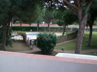 a swimming pool in a park with trees and a fence at Primera línea de playa casita adosada in Chiclana de la Frontera