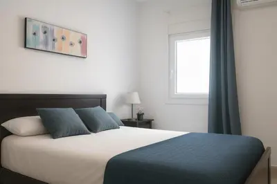 a bedroom with a bed with blue and white sheets and a window at Apartamento sureño in Cádiz