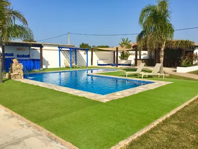 a swimming pool with green grass next to a house at EL ALAZAN in Chiclana de la Frontera