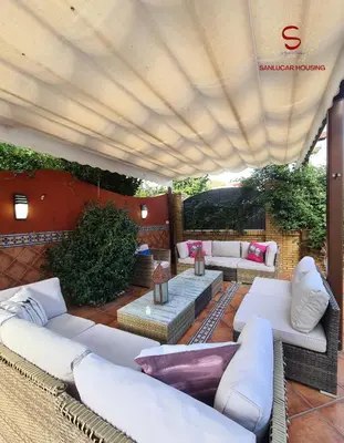 a patio with white couches and tables and a large umbrella at Casa Hermosilla con piscina by Sanlúcar Housing in Sanlúcar de Barrameda