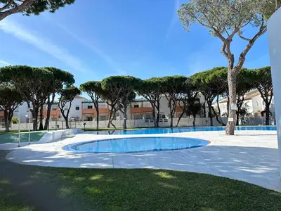 a swimming pool in the middle of a park with trees at Dúplex Playa Sol Ostra in Chiclana de la Frontera