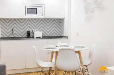 a white kitchen with a table and white chairs at Estudio Gaviota by Cadiz Time in Cádiz
