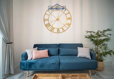 a blue couch in a living room with a clock on the wall at Apartamento Diego Benitez in Sanlúcar de Barrameda