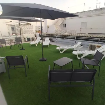 a group of chairs and an umbrella on the grass at Hostal Sevillana Costa in Chipiona