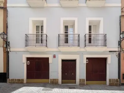 a facade of a white building with three garage doors at El Rincón de Fabio Little Apartments in Cádiz