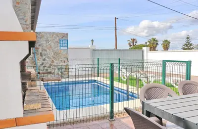 a swimming pool behind a fence with a table and chairs at Villa Ana in Conil de la Frontera