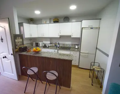 a kitchen with white cabinets and a counter with stools at Apartamento Residencial Al Andalus 117, La Barrosa, Chiclana, Incluye parking a unos metros del mar in Chiclana de la Frontera