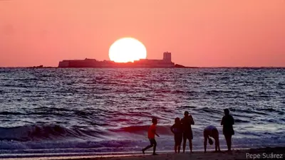 a group of people standing on the beach at sunset at Apartamento Residencial Al Andalus 117, La Barrosa, Chiclana, Incluye parking a unos metros del mar in Chiclana de la Frontera