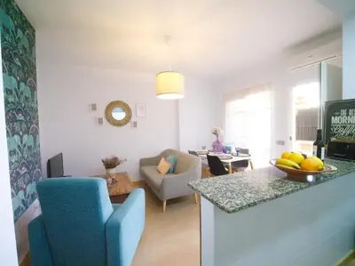 a kitchen and living room with a blue chair and a table at Apartamento Residencial Al Andalus 117, La Barrosa, Chiclana, Incluye parking a unos metros del mar in Chiclana de la Frontera