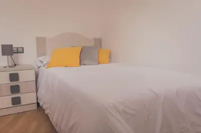 a white bed with yellow pillows and a night stand at Apartamentos Puerta Sevilla in Jerez de la Frontera