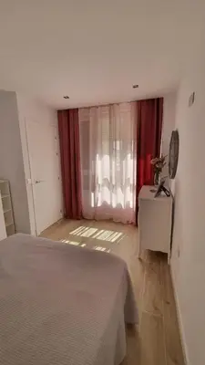 a bedroom with a bed and a window with red curtains at APARTAMENTO A PIE DE PLAYA. in Cádiz