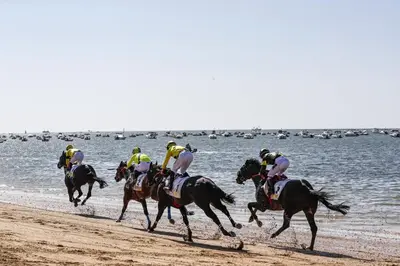 a group of jockeys riding horses on the beach at Atico Capuchinos in Sanlúcar de Barrameda